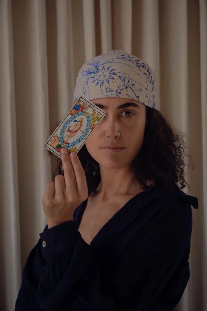 María Posada, astróloga y tarotista, fundadora de Astarot y de la escuela Casa Alquimia, sosteniendo la carta El Mundo del Tarot de Marsella
